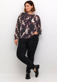 Flowy, multicolored blouse with a dark, abstract pattern, round neckline, and long sleeves, paired with black fitted pants and glossy shoes.