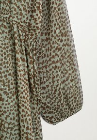 Blouse à motifs verts avec imprimé léopard marron, manches froncées et cordon de serrage à la taille pour un ajustement personnalisé.