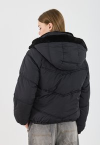 Zwarte pufferjack met capuchon, voorzien van een gevoerde kraag, gequilt ontwerp en elastische onderkant. Draag het over high-waisted grijze jeans.