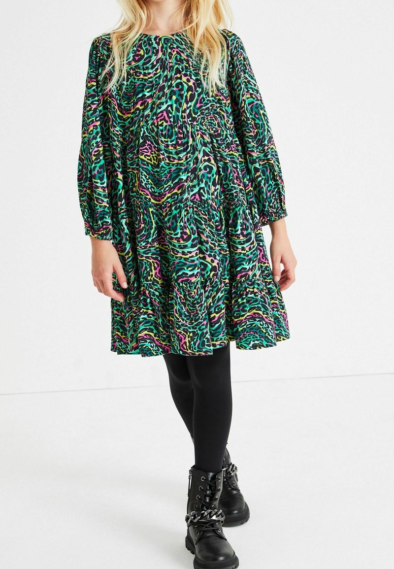 Zelené šaty s potiskem a růžovými a černými akcenty; dlouhé vycpané rukávy, nařasený pas a rozšířená sukně. Nosené s černými legínami a botami.