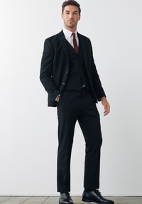Black suit with a fitted, tailored design, featuring a three-button vest, white shirt, and red tie. Glossy black dress shoes complete the look.