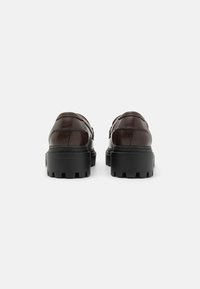 Brown leather shoes with a sleek design, featuring a chunky black rubber sole and detailed stitching on the upper. Rear view shown.