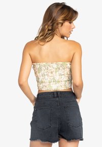 Strapless blomster crop top i lyse farver med grønne og ferskenmønstre, parret med højtaljede sorte denim shorts med frynset kant.