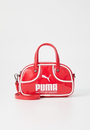 Červená lesklá kabelka Puma s bílým lemem, dvojitými úchyty, odnímatelným popruhem a bílým logem Puma s německým textem na přední straně.