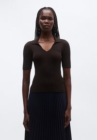 Top de punto marrón con textura acanalada, manga corta y escote en V, con cuello y diseño ajustado. Combinado con una falda plisada azul marino.