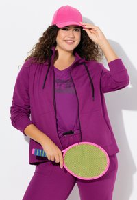 Fialový sportovní outfit se zipovou bundou, krátkým rukávem a pásem na stažení. Doplněný růžovou čepicí a držící růžovou a zelenou pádlo.
