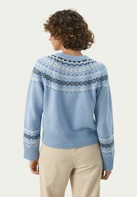 Light blue knitted sweater featuring a patterned yoke in black and white, ribbed cuffs, and hem. The design includes geometric shapes.