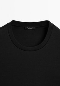 Černé bavlněné tričko s kulatým výstřihem a žebrovanými detaily. Etiketa zní "Massimo Dutti" s nápisem "Vyrobeno v Portugalsku" pod ním.