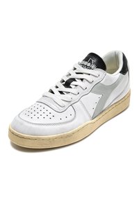 Sneaker bianca in suede con un pannello laterale grigio testurizzato, accenti neri sul tallone e sulla linguetta, punta perforata e suola in gomma crema.