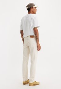 Witte denimjeans met een rechte snit, voorzien van een leren achterlabel in bruin, gedragen met een wit T-shirt en tan kleurige schoenen.