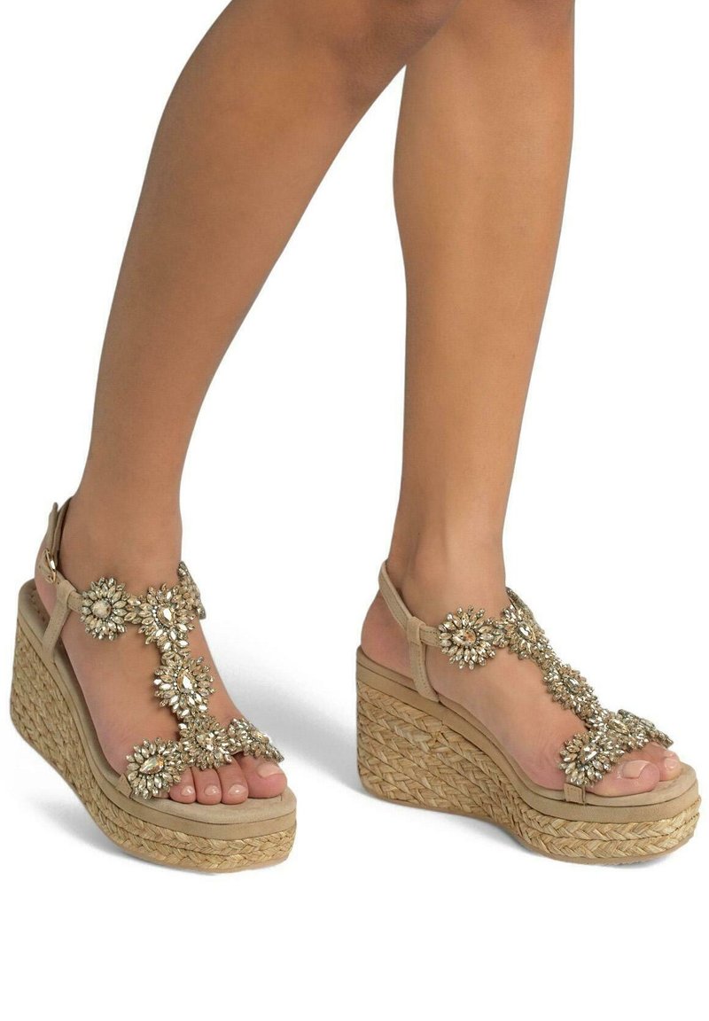 Sandales à talon compensé beige avec des accents de gemmes décoratives, des détails en jute tissé, un design à bout ouvert et des brides de cheville. Surface texturée et embellissements floraux.
