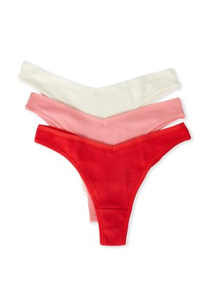 Trois strings pour femmes en tissu côtelé en blanc, rose clair et rouge, superposés sur un fond blanc.