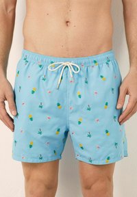 Costume de baie albastre cu talie elastică și șnur ajustabil. Prezintă un design brodat multicolor cu ananași, băuturi și palmieri.
