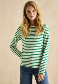 Zaļa un balta svītrainā, garām piedurknēm krekls, kas izgatavots no mīksta auduma, ar apaļu izgriezumu un nelielu logotipa detaļu uz piedurknes.