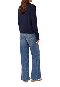 Marineblauwe trui met geribbelde manchetten, gecombineerd met lichtblauwe wijde jeans. De stof heeft een zachte textuur en een losvallende pasvorm, aangevuld met lichtbruine schoenen.