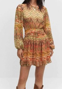 Vestido de manga larga, con estampado de paisley en tonos naranja, amarillo y verde. Cintura con volantes y falda acampanada en una tela texturada.