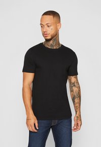 Schwarzes kurzärmliges T-Shirt aus glattem Baumwollstoff, mit Rundhalsausschnitt und taillierter Passform. Getragen mit blauen Jeans.
