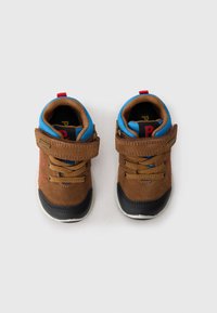 Chaussures pour tout-petits en suède marron avec des accents bleus, un capuchon en caoutchouc noir à l'avant, et des coutures rouges. Elles possèdent une sangle Velcro et un design à lacets.