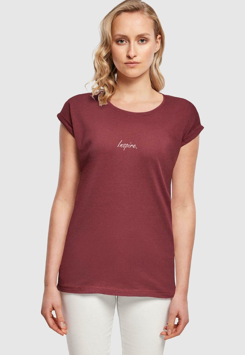 Maglietta in cotone borgogna con maniche arrotolate e scollatura rotonda, decorata con la parola "Inspire." ricamata in lettere chiare sul davanti.