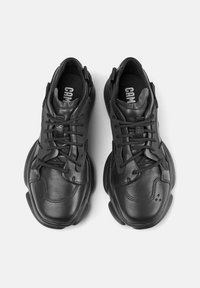 Black sneakers with leather upper, lace-up design, textured panels, and rubber soles. Accented with branding on the tongue and insole.