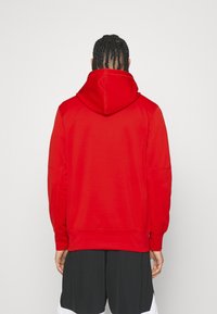 La sudadera con capucha roja presenta un diseño sólido, puños acanalados y detalles en la yugo trasero, confeccionada en una tela suave para mayor comodidad.