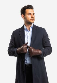 Brown leather gloves with stitched accents, worn by a person in a dark coat over a light blue striped shirt, standing against a white backdrop.