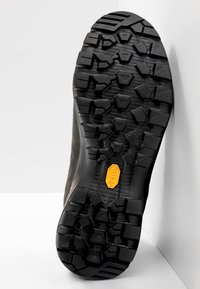 Czarna podeszwa buta trekkingowego z głębokim, wielokierunkowym bieżnikiem. Oznaczona żółtym logo Vibram i teksturowaną powierzchnią dla lepszej przyczepności.