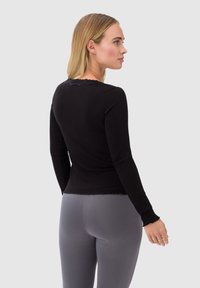 Czarny, długi rękaw top o prążkowanej fakturze i falbaniastym wykończeniu dekoltu, w połączeniu z dopasowanymi szarymi legginsami.
