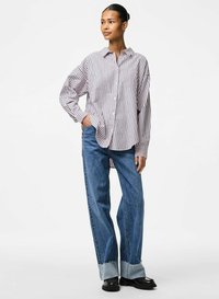 Camicia a righe con un fit morbido; sfumature di righe bianche e bordeaux. Abbinata a jeans blu a gamba larga con orli sfrangiati.
