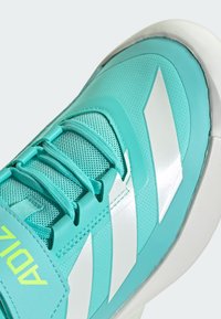 Scarpa da atletica turchese con tomaia strutturata, dotata di tre strisce bianche e design con lacci, accentuata da un logo neon.