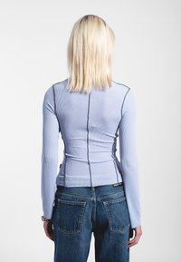 Light blue ribbed long-sleeve top with contrasting black stitching. The back features a center seam and is paired with high-waisted blue jeans.