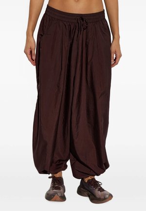 Pantaloni larghi marrone scuro con vita elastica e coulisse, indossati con scarpe sportive scure, mostrati sulla zona centrale e sulle gambe.