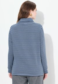 Maglietta a maniche lunghe con un motivo a righe blu e bianche, con colletto alto e texture morbida. Tessuto liscio, vestibilità comoda.