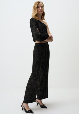 Zwarte, gemarmerde off-the-shoulder top gecombineerd met hoge taille, wijde broek met een subtiele glans, aangevuld met puntige hakken.