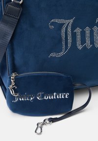 Granatowa torebka z zamszu z detalami z rhinestones i srebrnym metalicznym logo "Juicy Couture"; zawiera dopasowaną małą saszetkę z zapięciem.