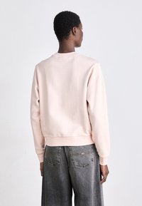 Világos rózsaszín pulóver, kerek nyakkal, puha anyagból készült, bordás mandzsettákkal és hem. Oversized szürke farmernadrággal párosítva.