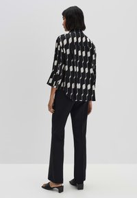 Camicia a righe in bianco e nero con vestibilità ampia, maniche lunghe e spalla a yoke. Abbinata a pantaloni neri e sandali con tacco.