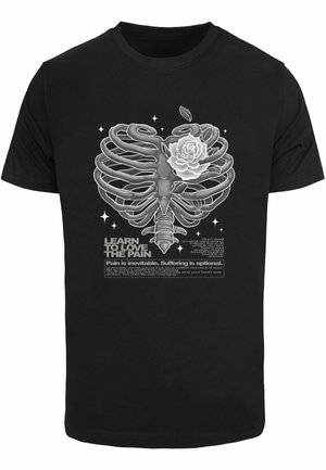 Schwarzes T-Shirt mit einer grafischen Darstellung eines Skelett-Rippenkäfigs, der mit einer weißen Rose verwoben ist, begleitet von Text und dekorativen Sternen.