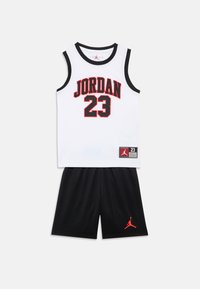 Άσπρο αμάνικο φανελάκι με κόκκινο κείμενο "JORDAN 23" και μαύρο περίγραμμα· συνδυάζεται με μαύρο σορτς που φέρνει κόκκινο λογότυπο Jumpman. Υλικό από βαμβακερό μείγμα.