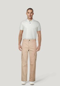 Beige cargobroek met zijzakken, knoopsluiting en een relaxte pasvorm, gecombineerd met een wit poloshirt met een kraag en zwarte knopen.