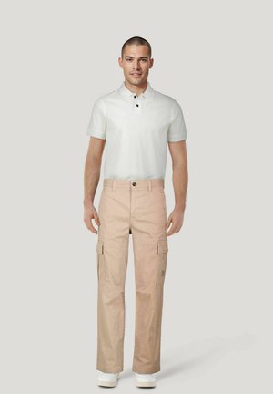 Beige cargobroek met zijzakken, knoopsluiting en een relaxte pasvorm, gecombineerd met een wit poloshirt met een kraag en zwarte knopen.