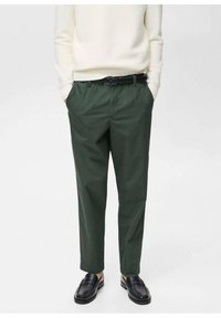 Green cotton trousers with a relaxed fit, featuring belt loops and side pockets. Paired with a white ribbed sweater and black loafers.