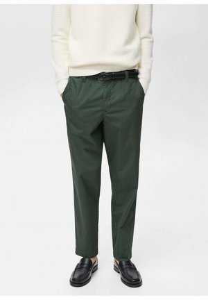 Pantaloni in cotone verdi con una vestibilità rilassata, dotati di passanti per la cintura e tasche laterali. Abbinati a un maglione bianco a coste e mocassini neri.