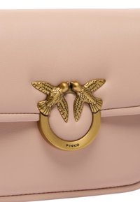 Růžová kožená kabelka se zlatavým uzávěrem, na kterém jsou dva ptáci, kulatým akcentem, hladkou texturou a minimalistickým designem.