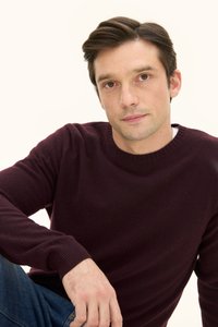 Bordeauxfarbener Pullover mit Rundhalsausschnitt und gerippten Bündchen, kombiniert mit blauen Denim-Jeans. Glatte Textur, taillierte Passform.