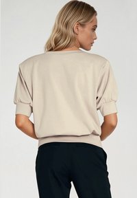 Beżowy sweter z krótkimi, bufiastymi rękawami i okrągłym dekoltem. Miękki materiał z dopasowanym dołem. Noszony z czarnymi, dopasowanymi spodniami.