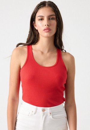 Top de tirantes rojo con canalé y tirantes anchos, corte entallado y escote redondo, combinado con jeans blancos de cintura alta.