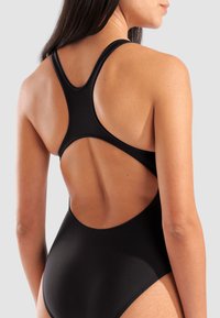 Maillot de bain une pièce noir avec une coupe haute et un dos nu. Fabriqué en tissu lisse avec une silhouette élégante et moulante.