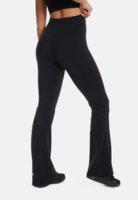 Black flared leggings made of stretch fabric, featuring a high waistband and a smooth texture. The design includes a small logo accent at the hem.