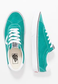 Tealfärgade mocka Vans-sneakers med vita snören, vita sulor och svart logotyp på innersulan och hälfliken, visade från ovan och sidan.